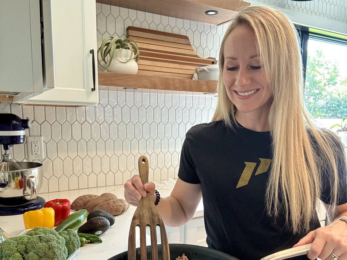 Monica Gleb cooking ground turkey in her kitchen, with peppers, broccoli and potatoes on the counter beside her